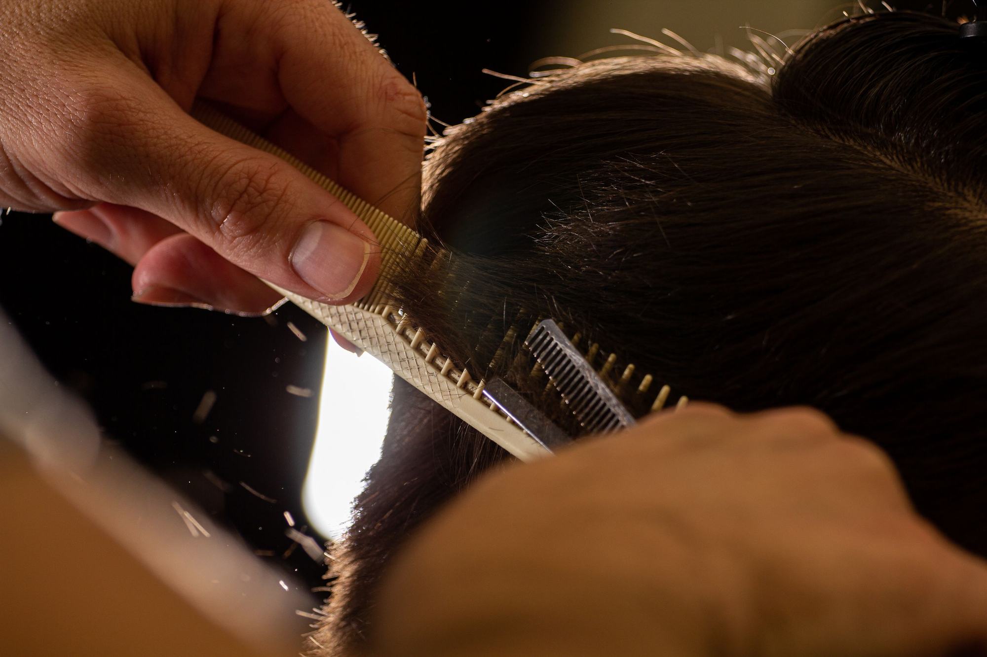 Licensed stock photograph: a stylist lifting a section of hair on a comb before cutting it.